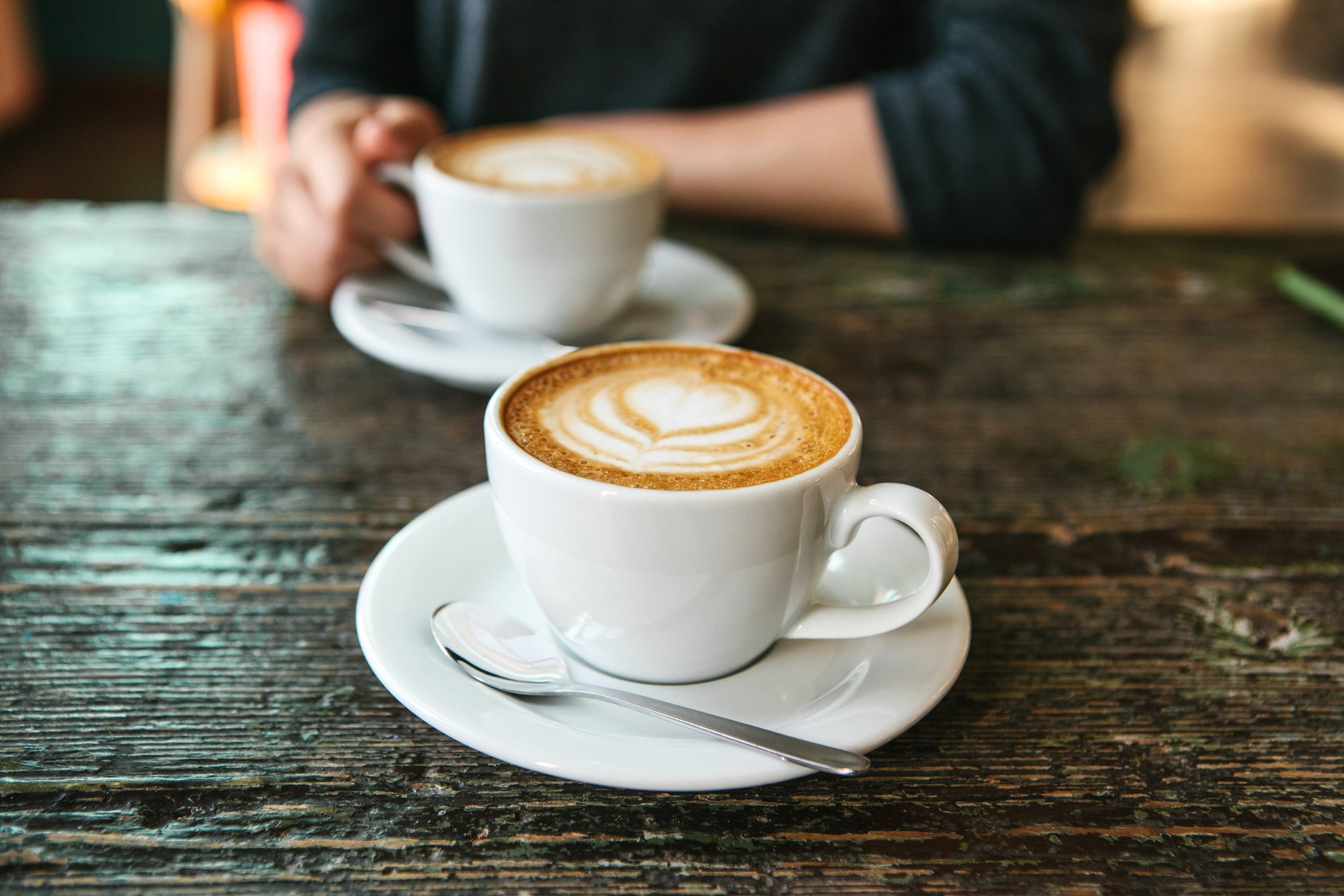Two mugs of barista-decorated coffee on a wooden table
