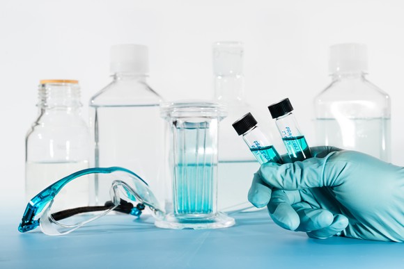 Hand holding two vials with blue liquid in front of lab glassware.