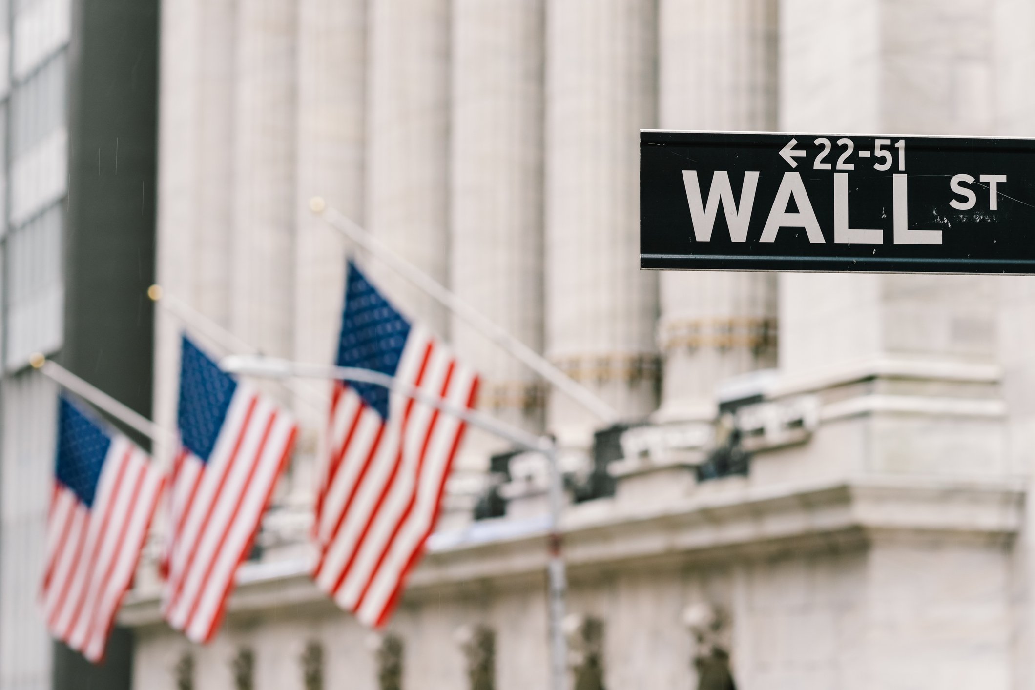 Wall Street sign with U.S. flags in front of the New York Stock Exchange in background