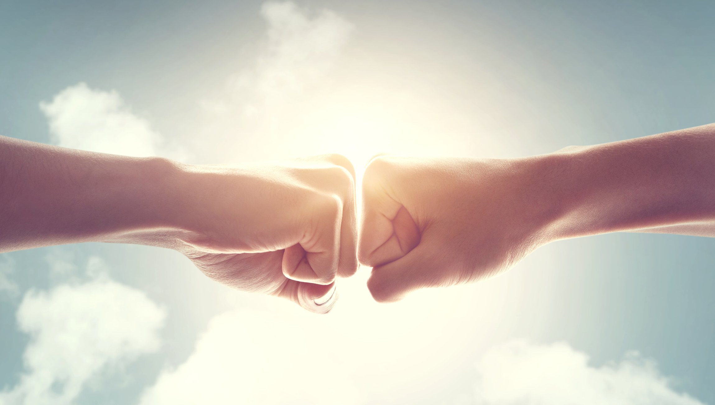 Two fists bumping against a blue sky background