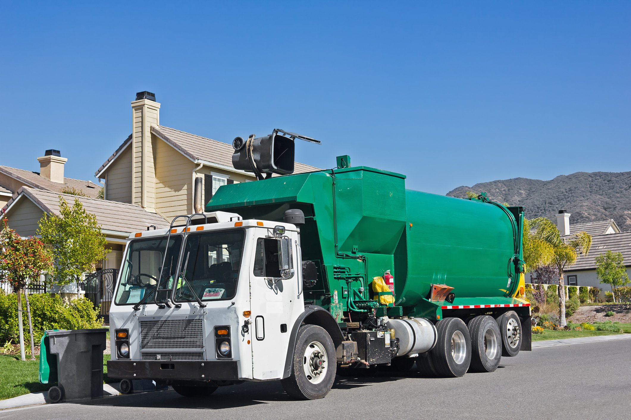 A garbage truck with a mechanical arm empties a trash bin
