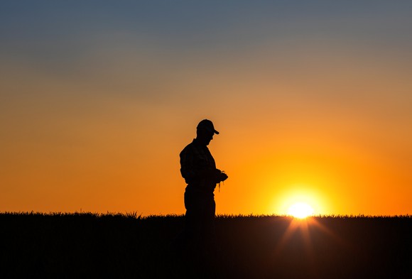 The silhouette of a farmer in the fields as sun goes down.
