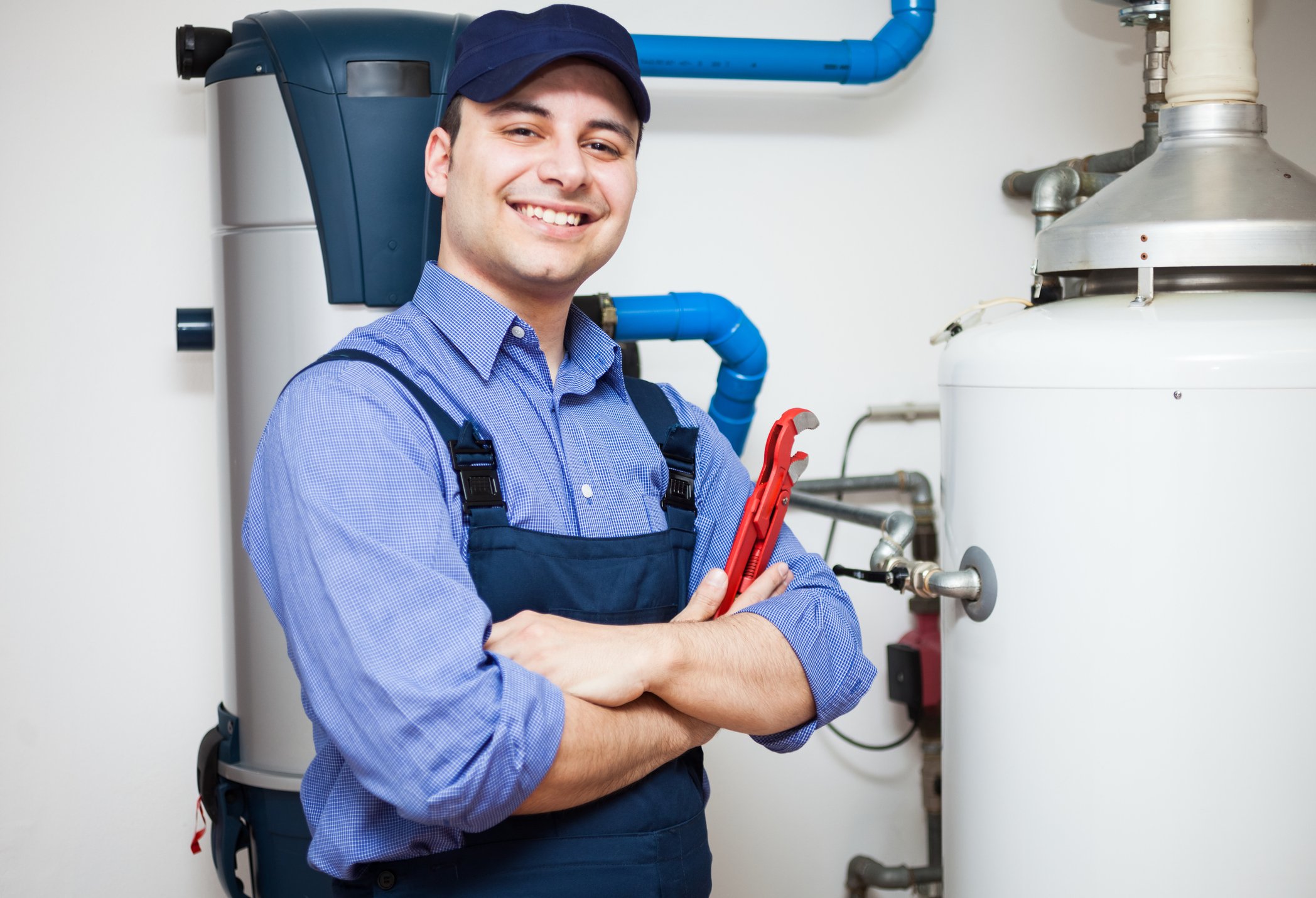 A smiling man holding a wrench stands next to a water heater