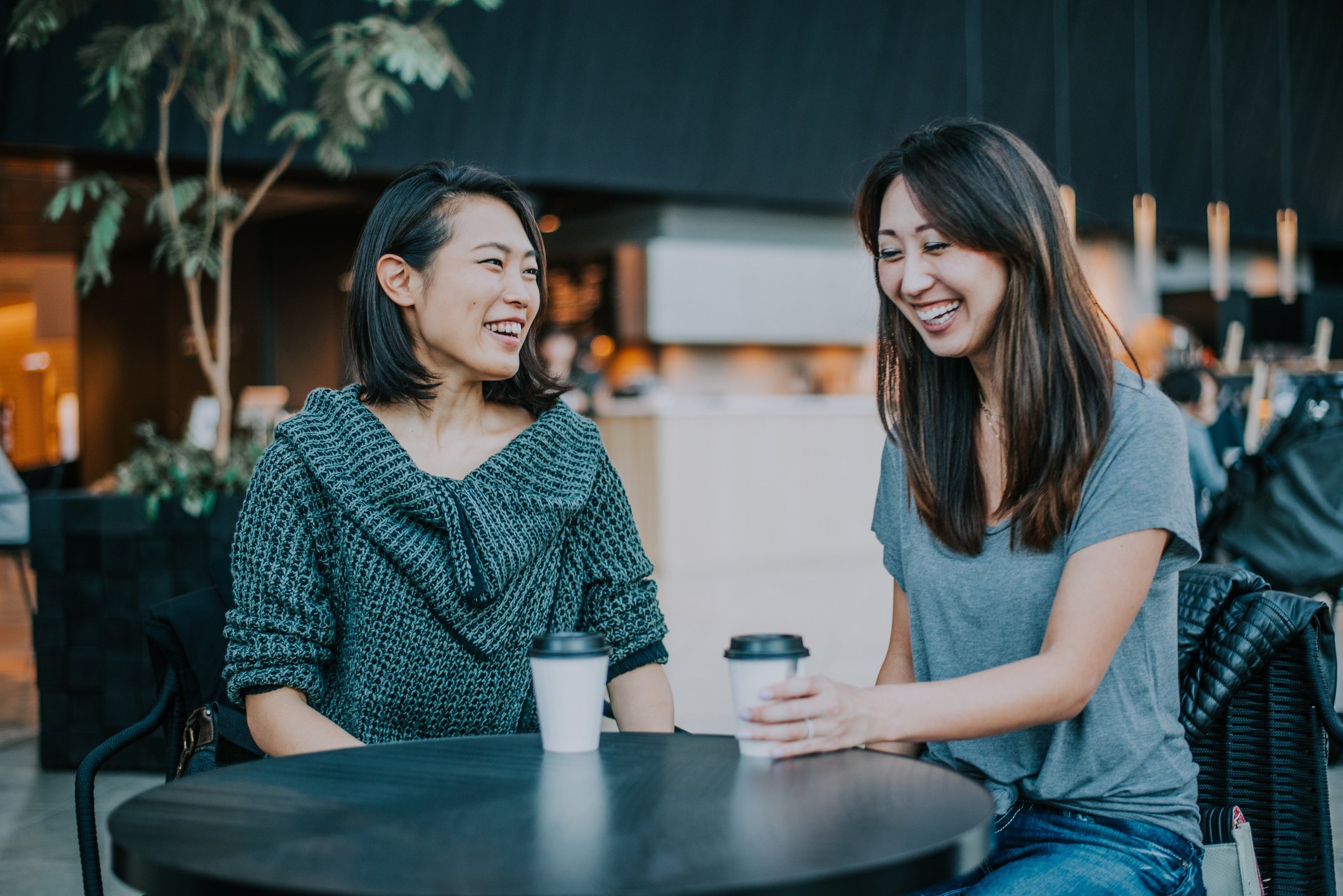 Two Asian women enjoying a cup of coffee.