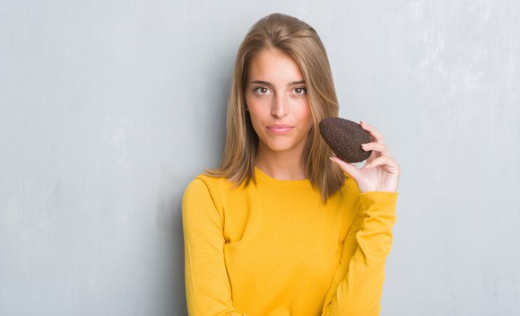 Young woman holds an avocado.