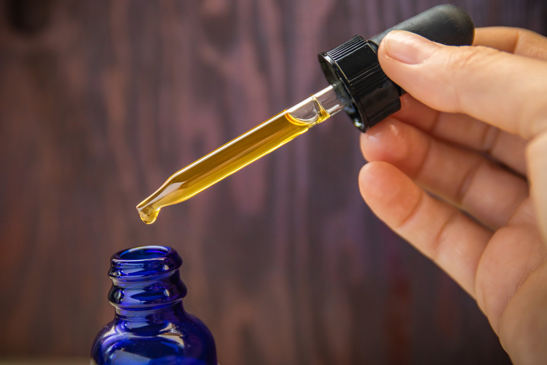 CBD oil vial with person holding dropper.