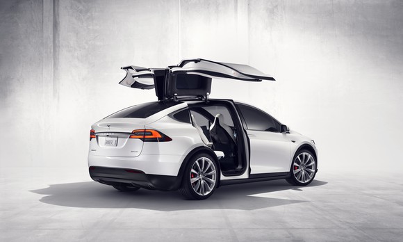 A white Tesla Model X with the falcon wing doors raised.