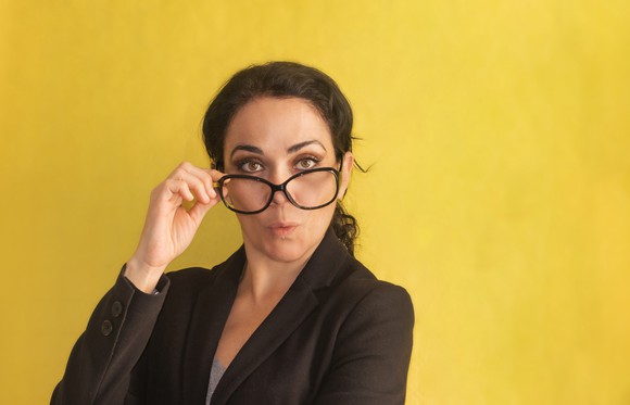 A professionally dressed woman peers over the top of her glasses with a look of surprise.