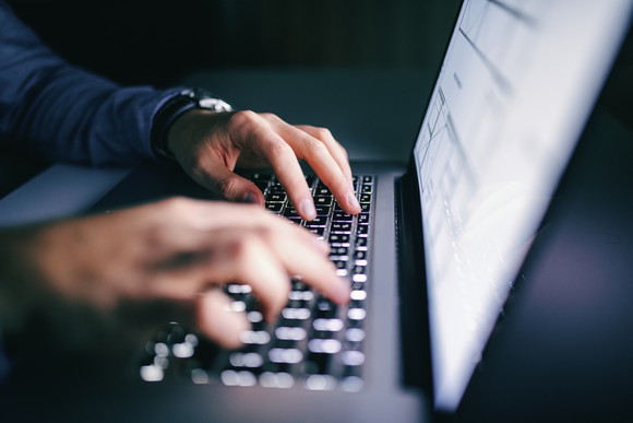A man's hands typing on a laptop with a report displayed on the screen.