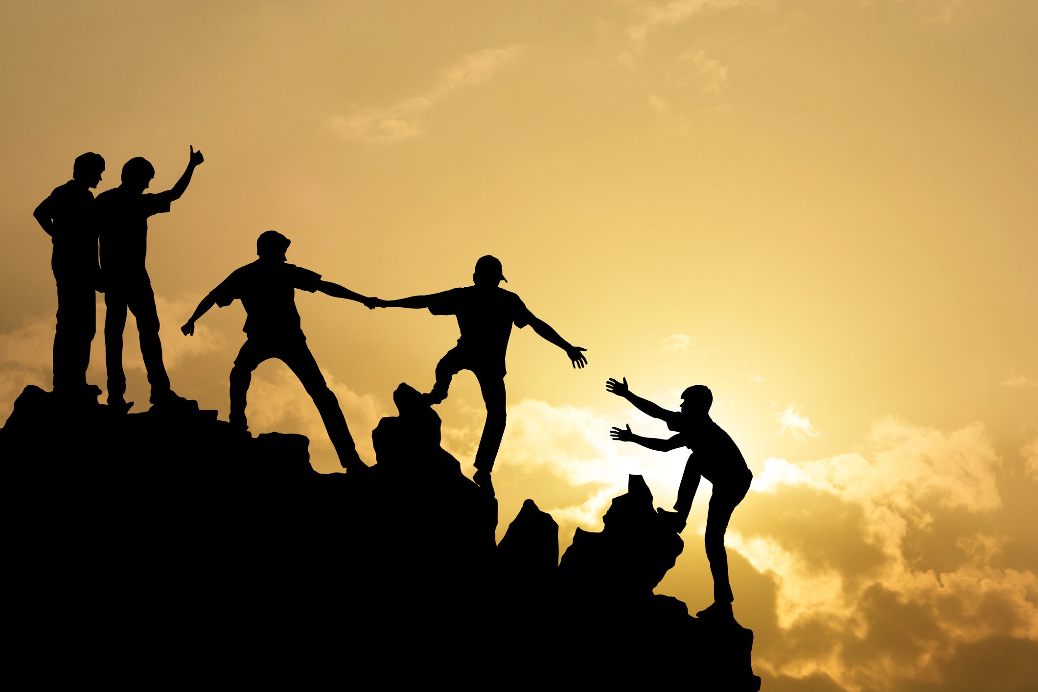 Silhouettes of several people helping each other climb a rocky hill or mountain, set against a bright yellow sunrise.