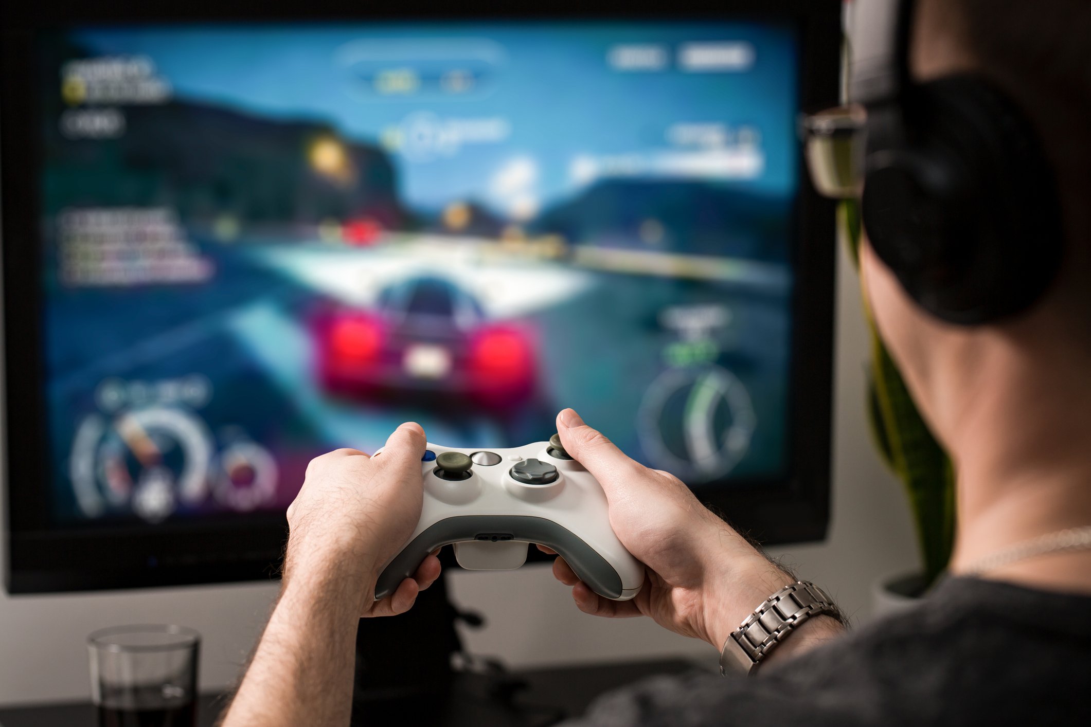 A video gamer holds a console controller in front of a screen, showing blurred images of a driving game.