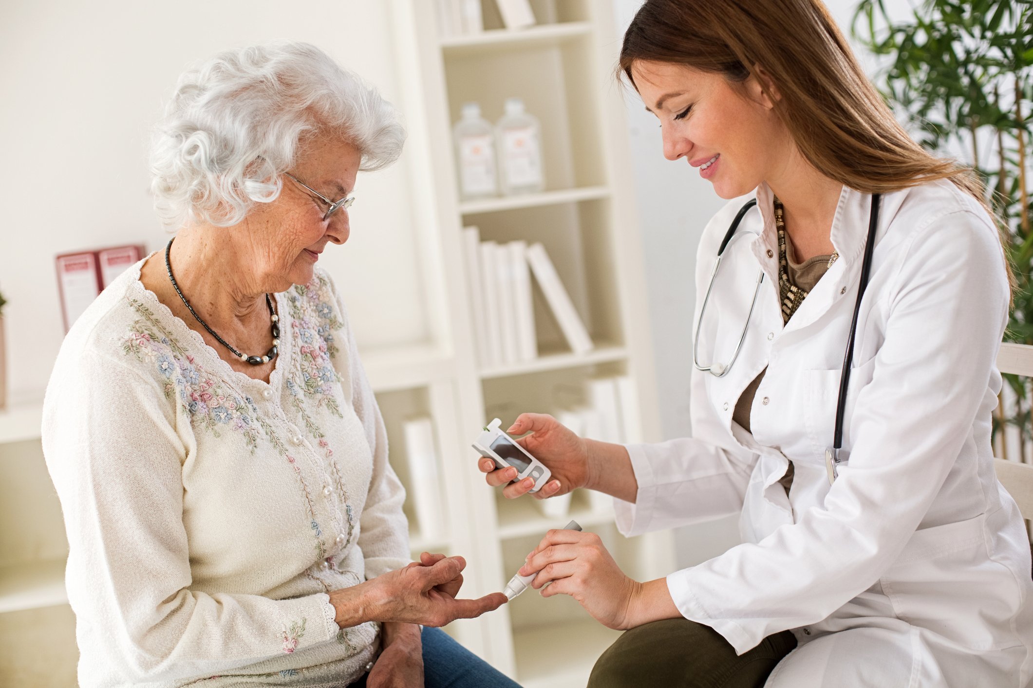 A female doctor checking the blood sugar of an elderly woman.