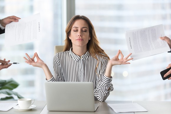 A woman meditating while sitting at a table with a laptop open to her