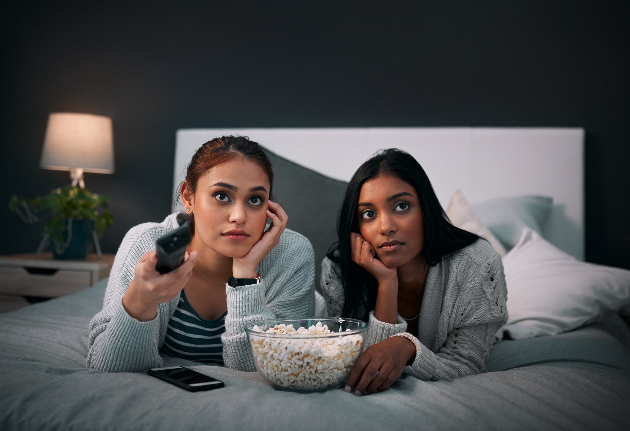 Two young women watching television, a bowl of popcorn between them