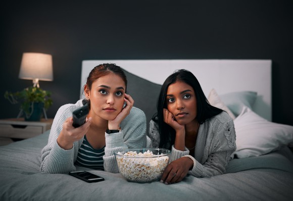 Two young women watching television, a bowl of popcorn between them