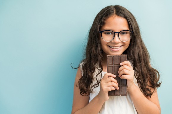 A young girl smiles as she holds a large chocolate bar.