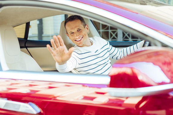 Older man waving from a nice car.