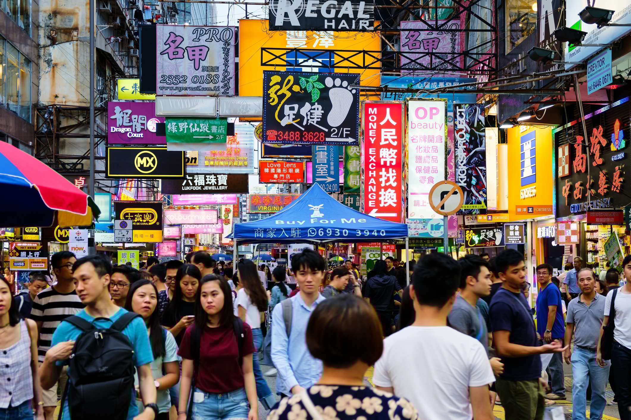 A very busy and crowded street in a Chinese city with signs crowding overhead above the people. 