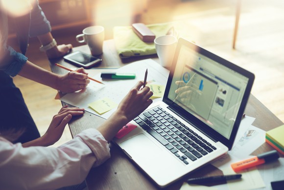 Two people working on research at a desk with papers and a notebook computer.