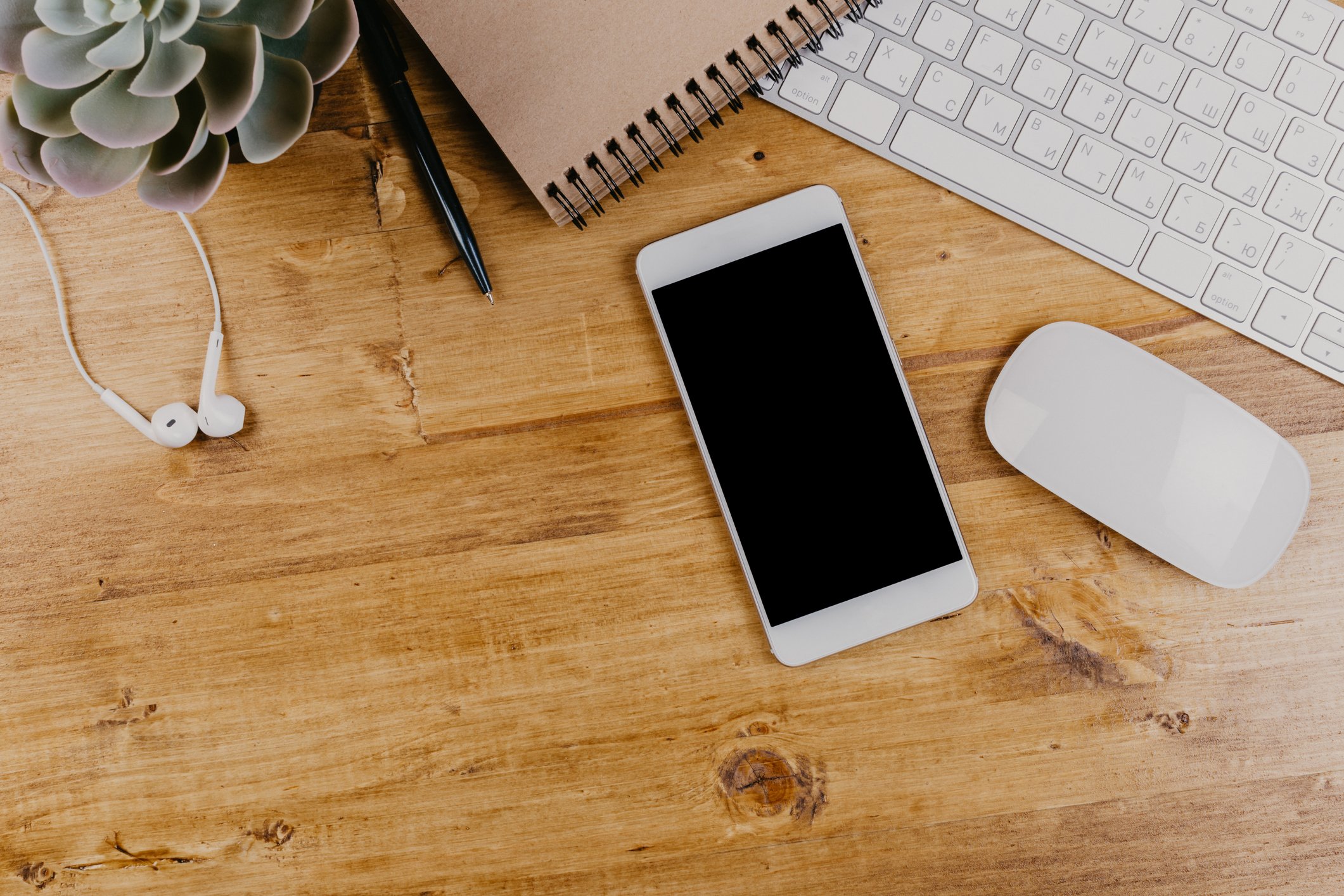 White headphones, iPhone, and laptop on a wooden desk