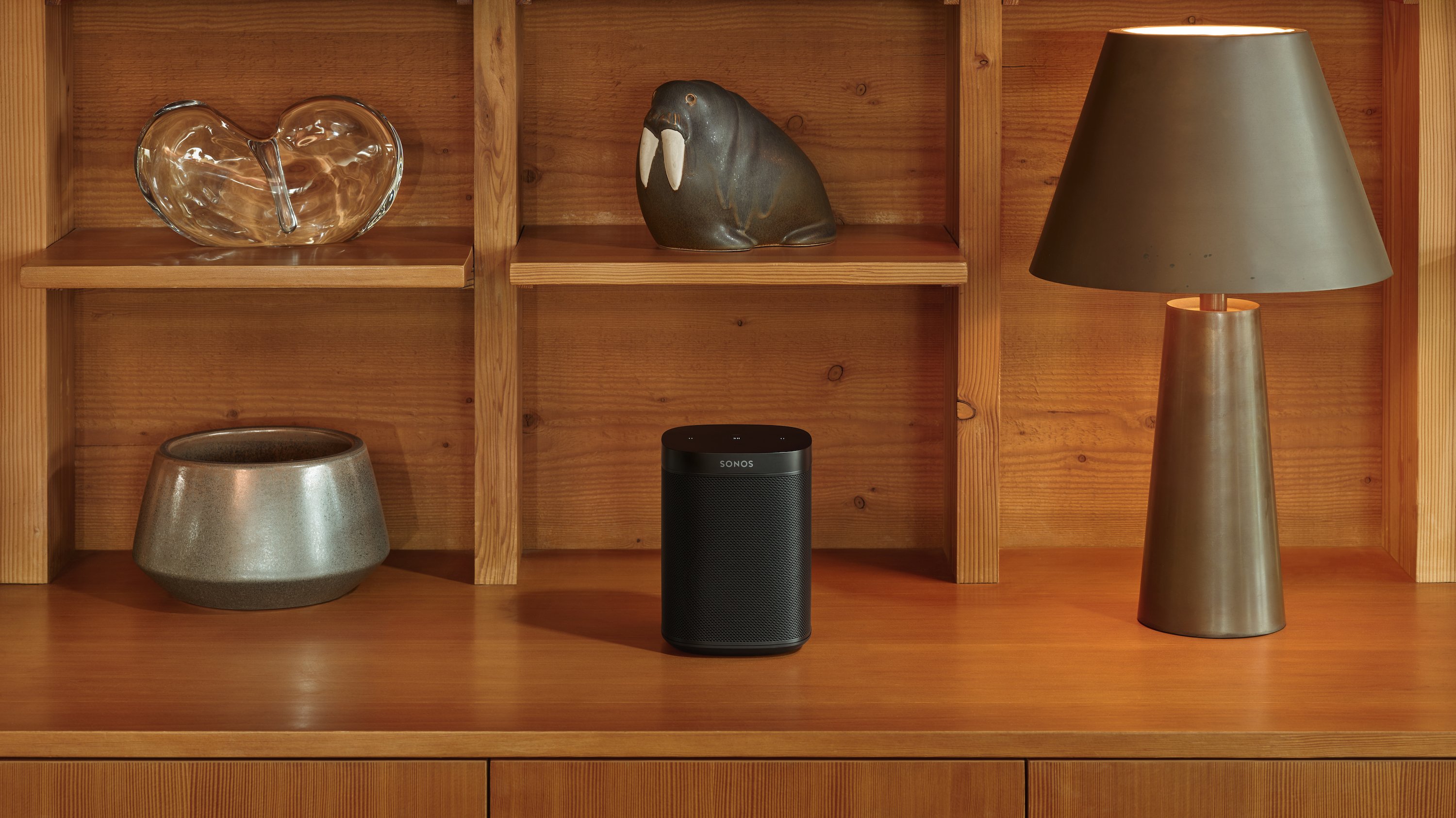 Sonos One SL on a shelf next to a lamp and a bowl