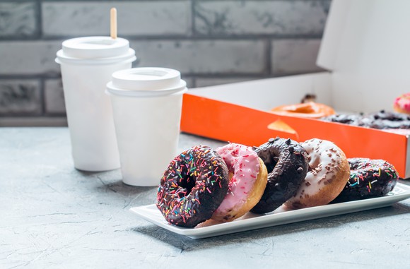 A box of doughnuts with cups of "to go" coffee.
