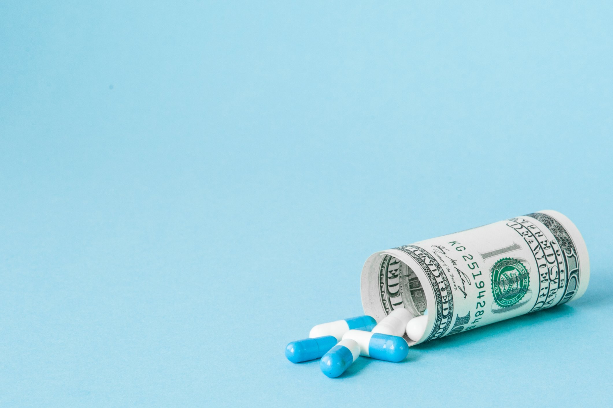 Blue and white pills spill out of a rolled dollar bill. 