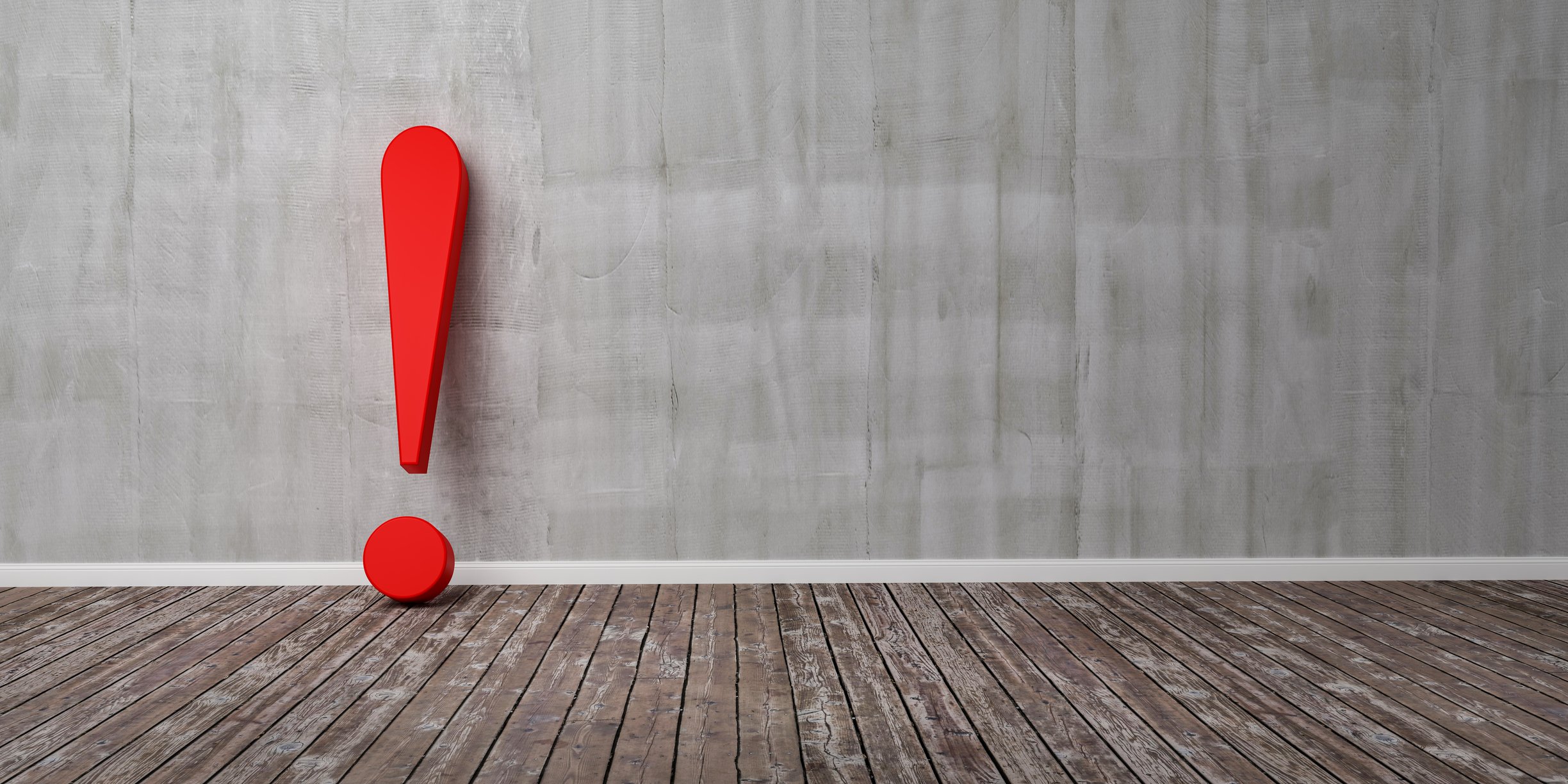 A red exclamation mark on a wooden floor, leaning up against a concrete wall. 