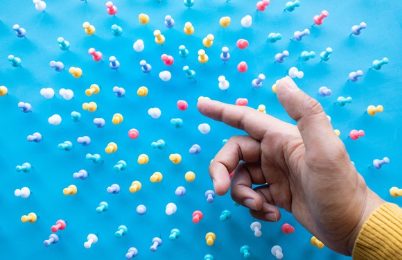 Finger pointing at pushpins on a blue field