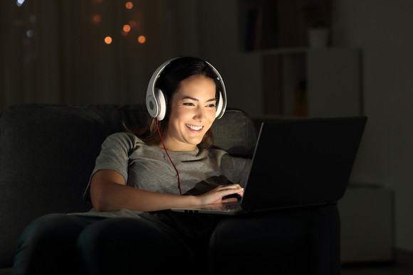 A woman wearing headphones and looking at a laptop in a dark room