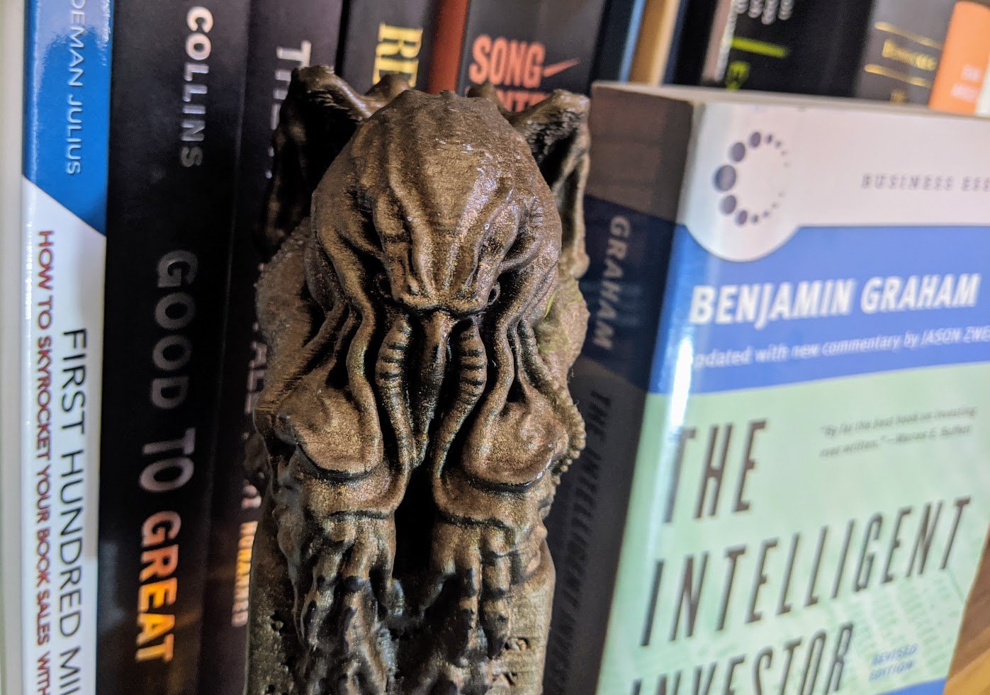 A 3D-printed Cthulhu statuette stands on a bookshelf between several great books about investing.