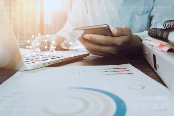 A person using a laptop and looking at a smartphone.
