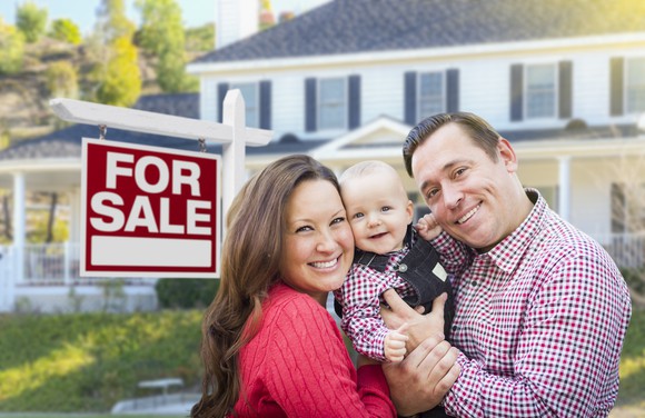 Smiling family in front of a home with a For Sale sign