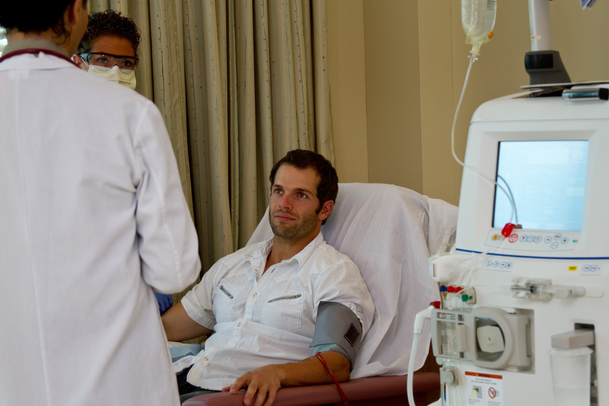 Man sitting in chair hooked to dialysis machine with a healthcare professional facing him.