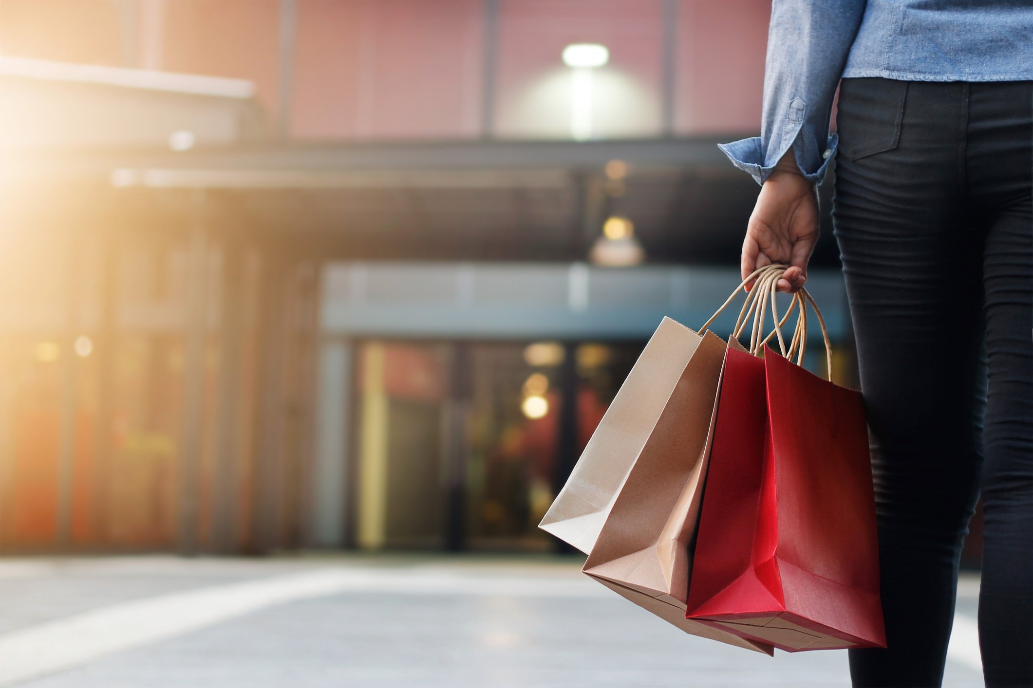 Person holding shopping bags, walking toward a mall entrance. 