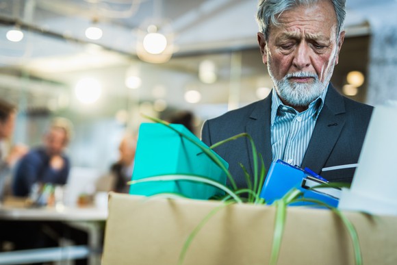 An older person in a suit packing his belongings in a cardboard box.