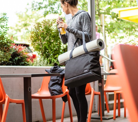 A woman carrying a Yeti soft-sided tote and a yoga mat.