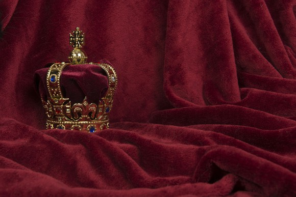 An ornate crown displayed against a purple fabric.