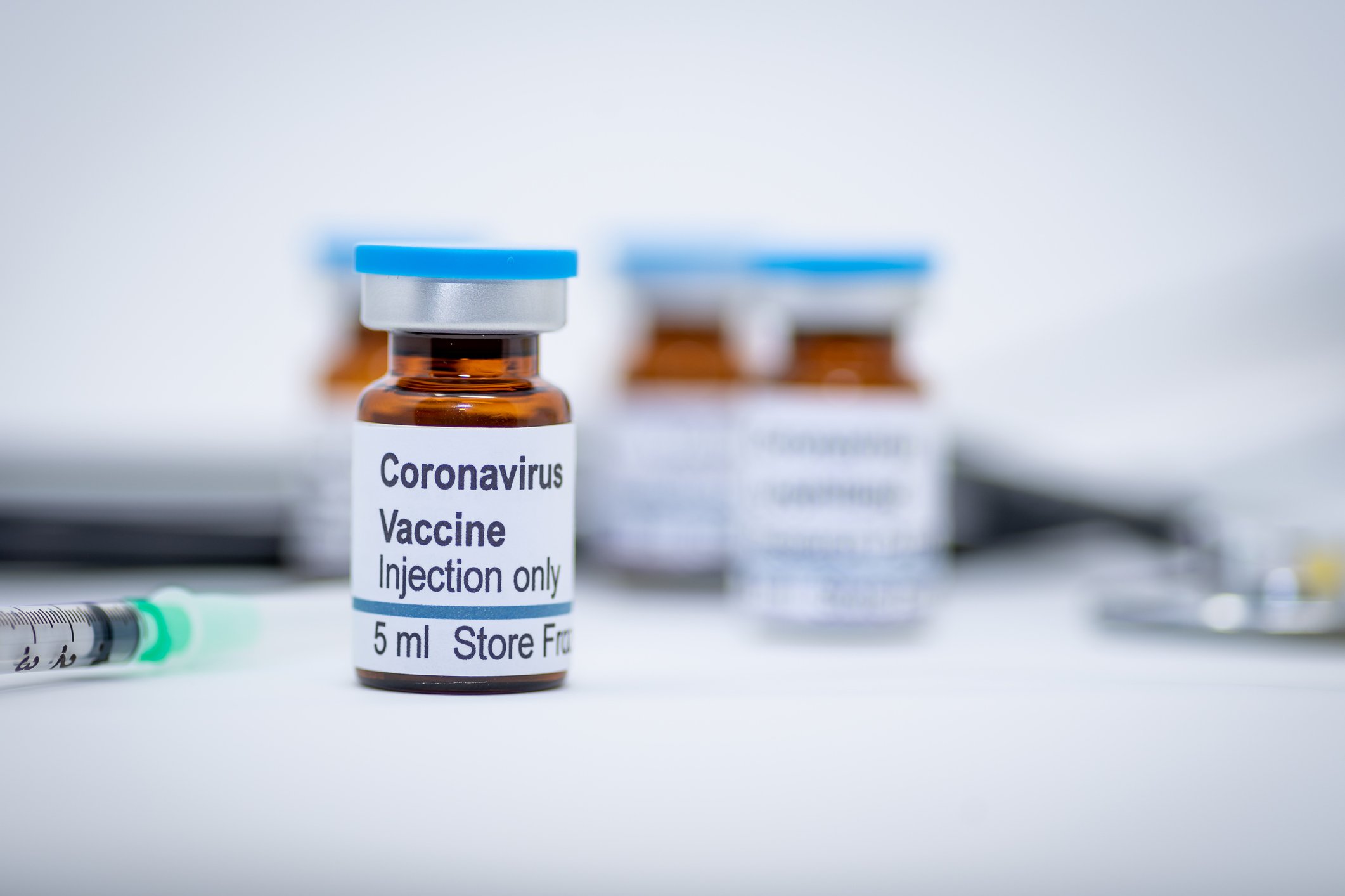 A vial labeled as a coronavirus vaccine sits on a table with other vials and a syringe