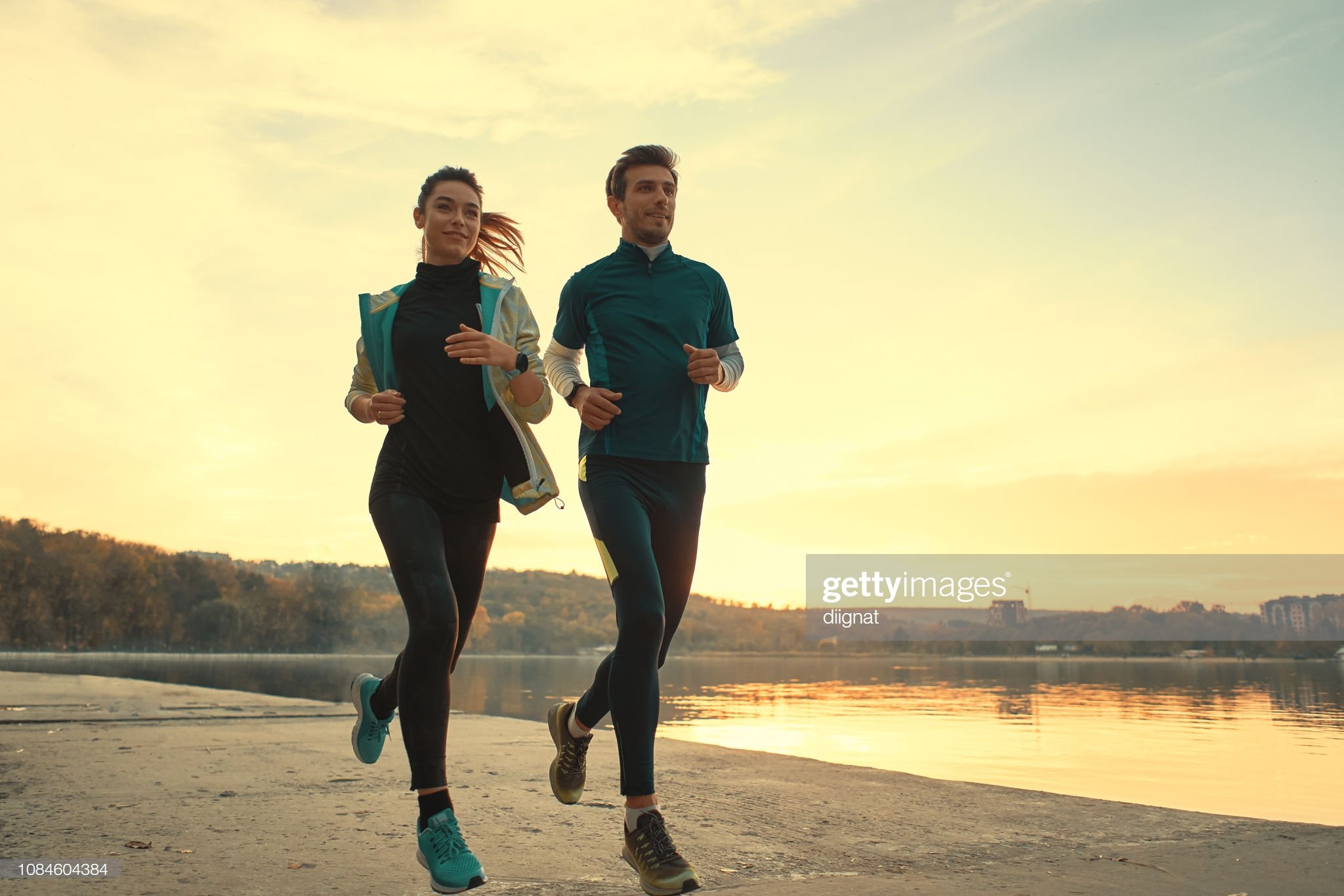 Young woman and young man running along a lake at sunrise of sunset.