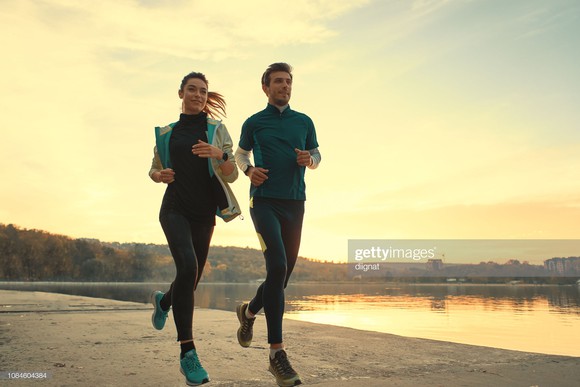 Young woman and young man running along a lake at sunrise of sunset.