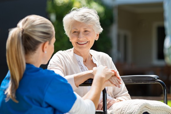Seated outdoors, a healthcare provider speaks with a smiling older woman.