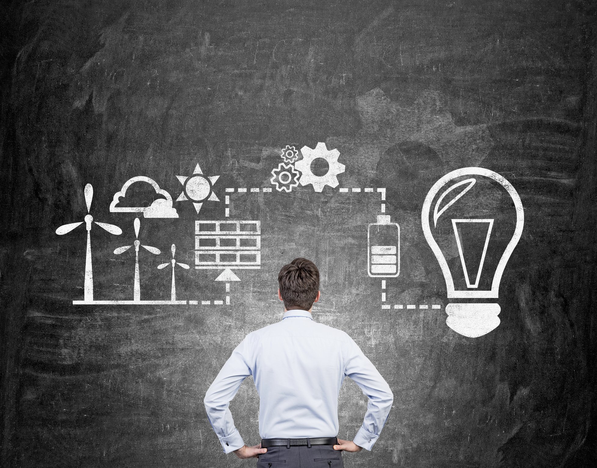 A man looks at illustrations of renewable energy sources on a chalkboard.