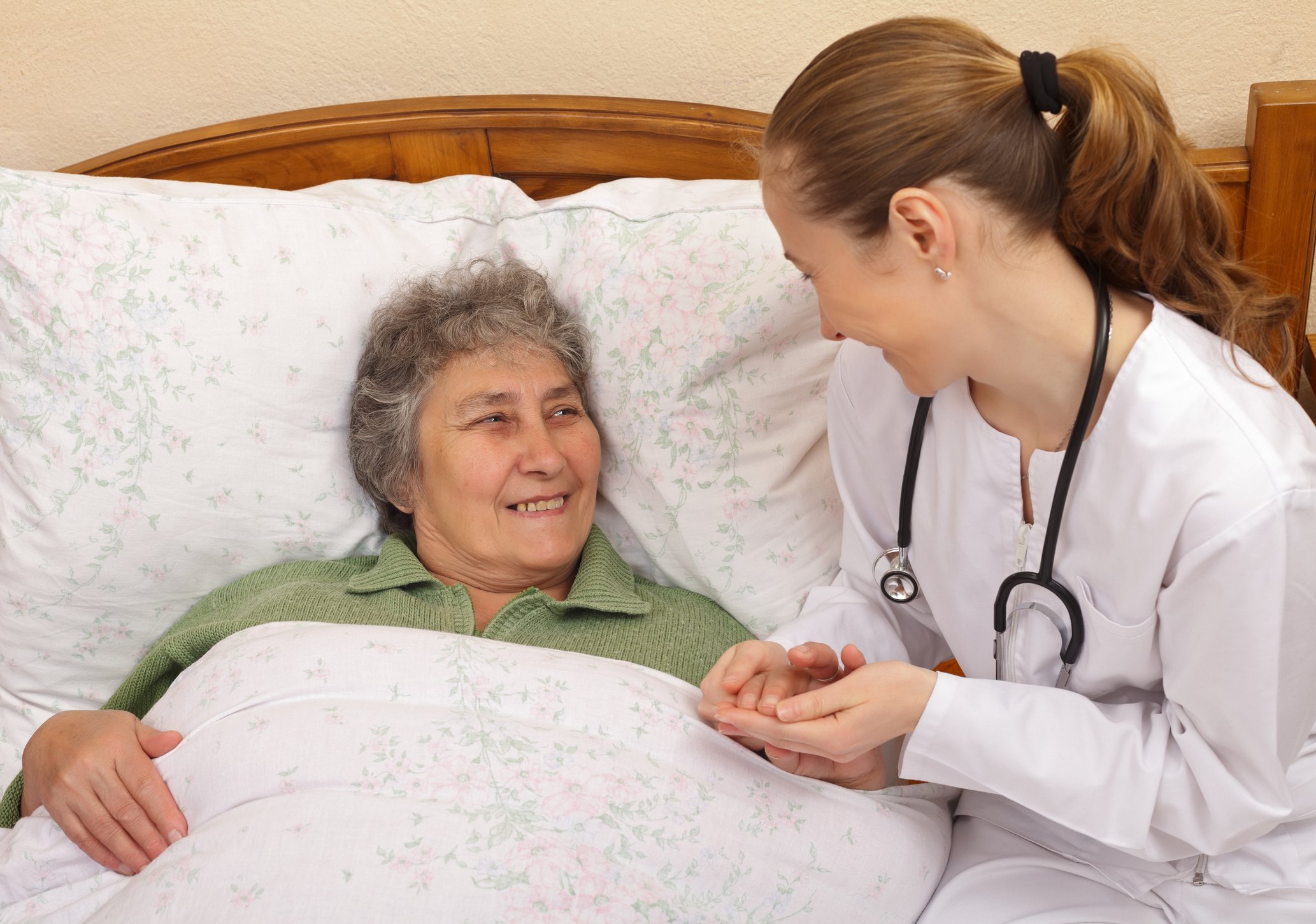 Nurse holding the hand of a smiling senior citizen who is lying in bed