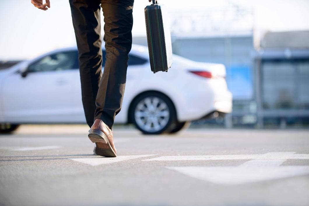 Person carrying briefcase walking toward a white car.