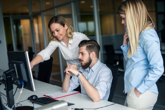Three office workers gathered around a computer monitor in an office.