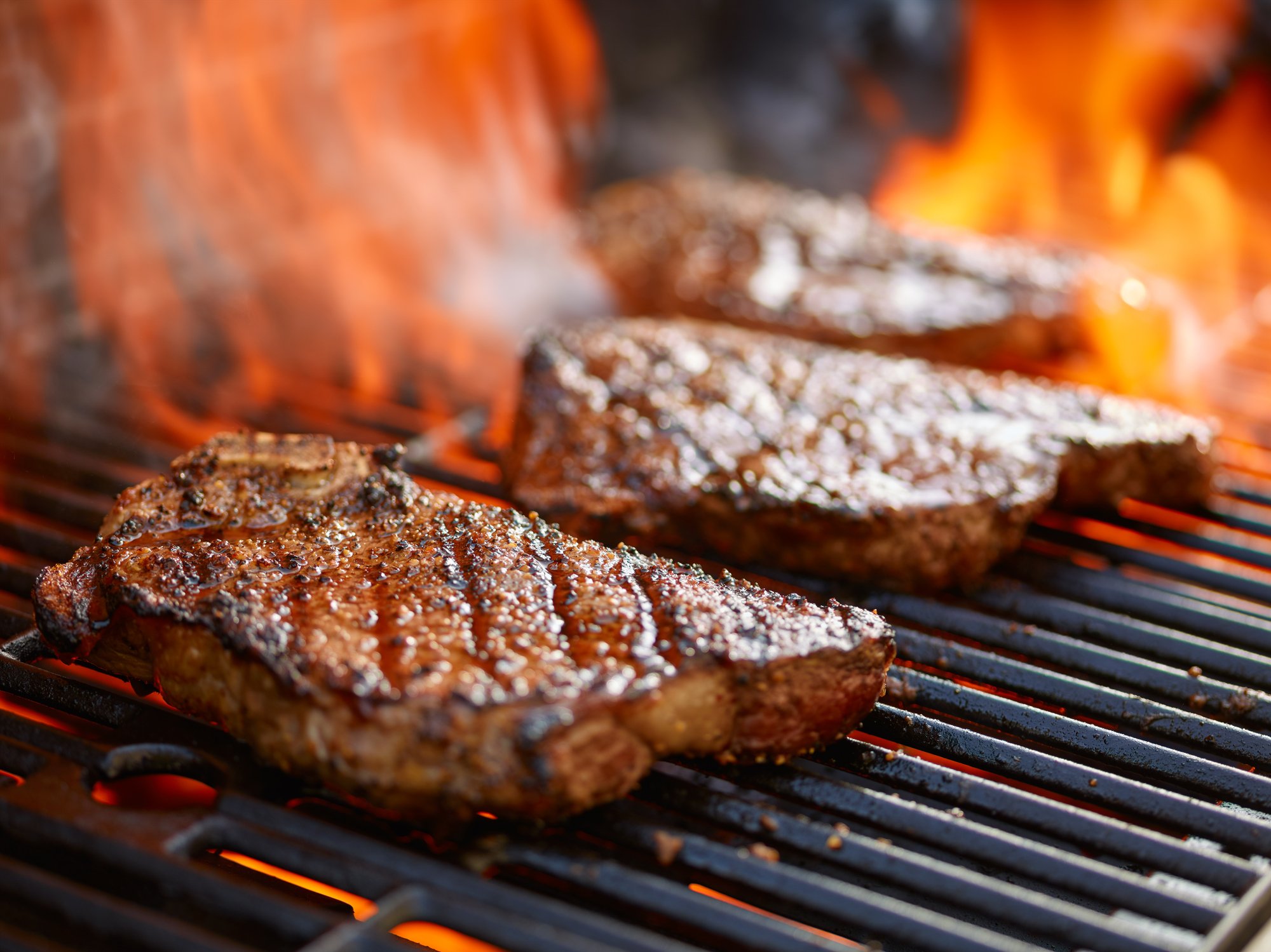 Three steaks cooking on a grill
