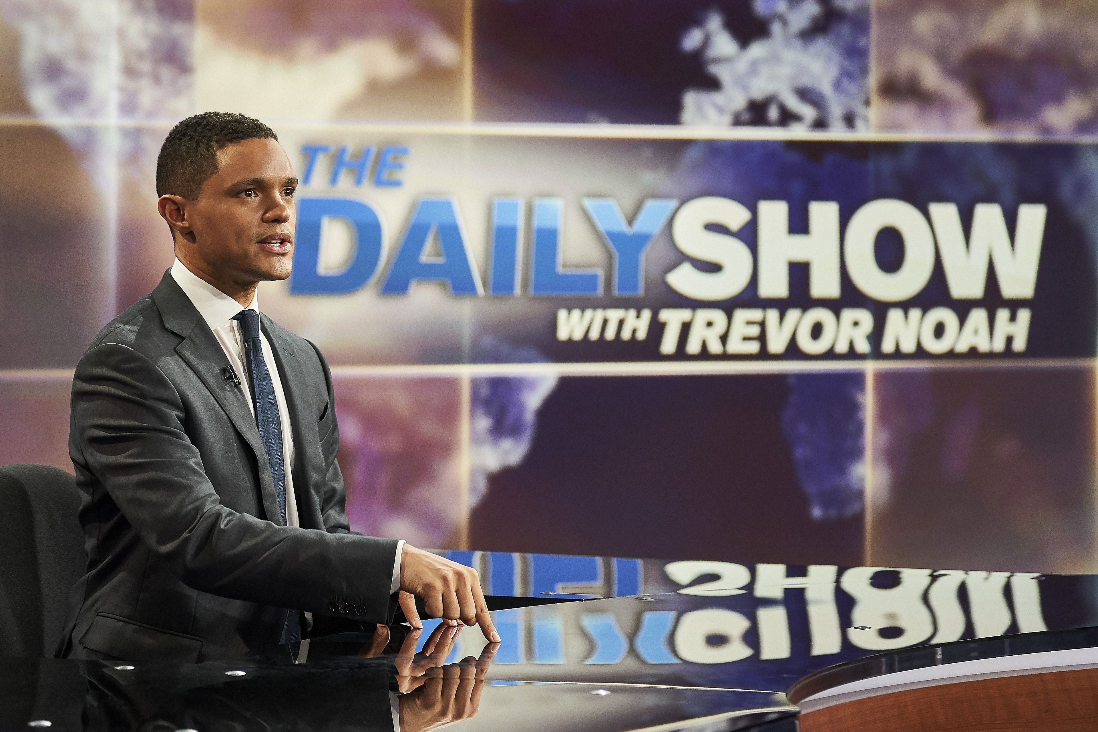 Daily Show host Trevor Noah sitting at a desk.