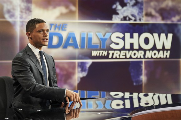Daily Show host Trevor Noah sitting at a desk.