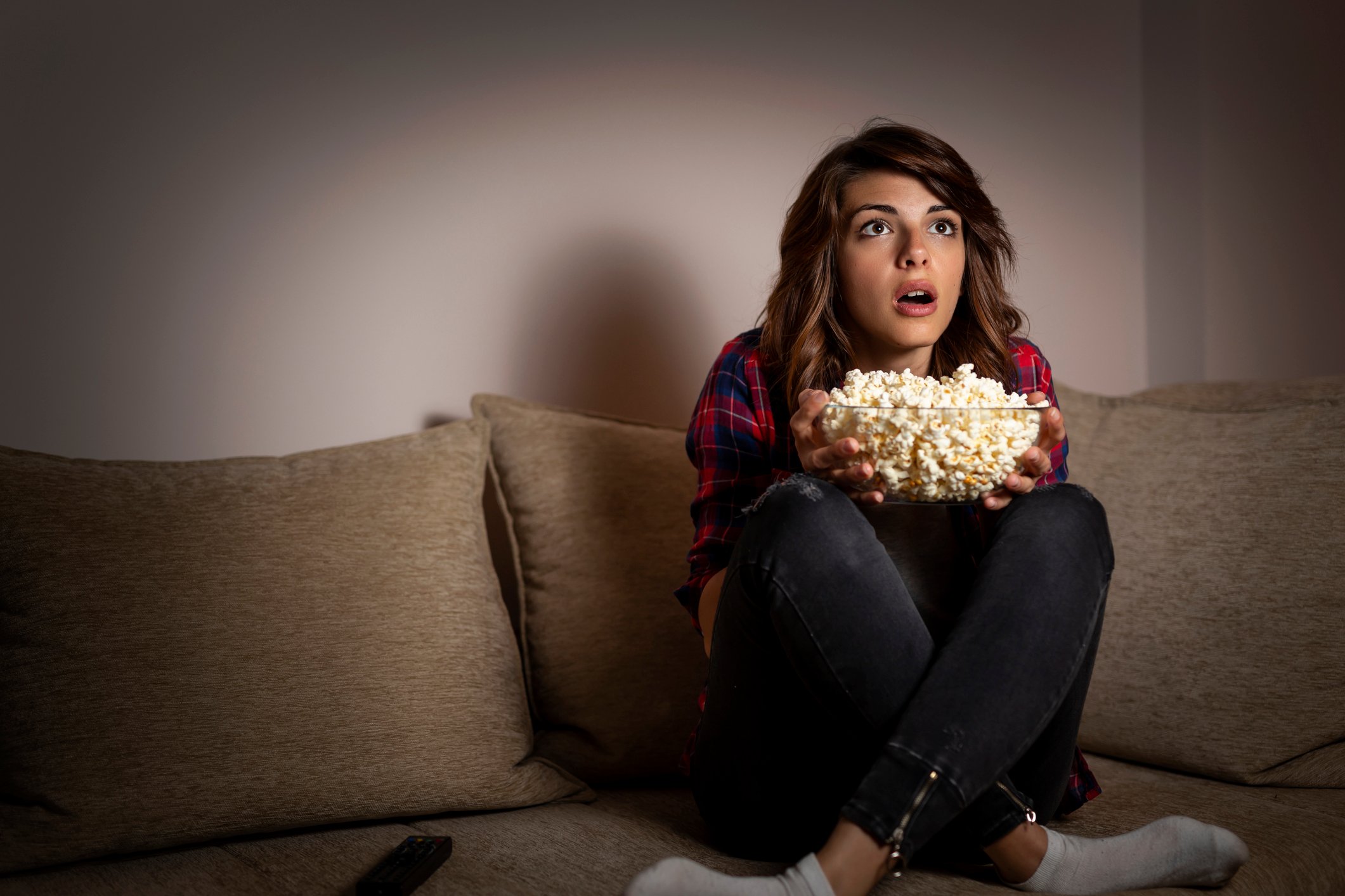 A girl sitting on the couch with a bowl of popcorn.